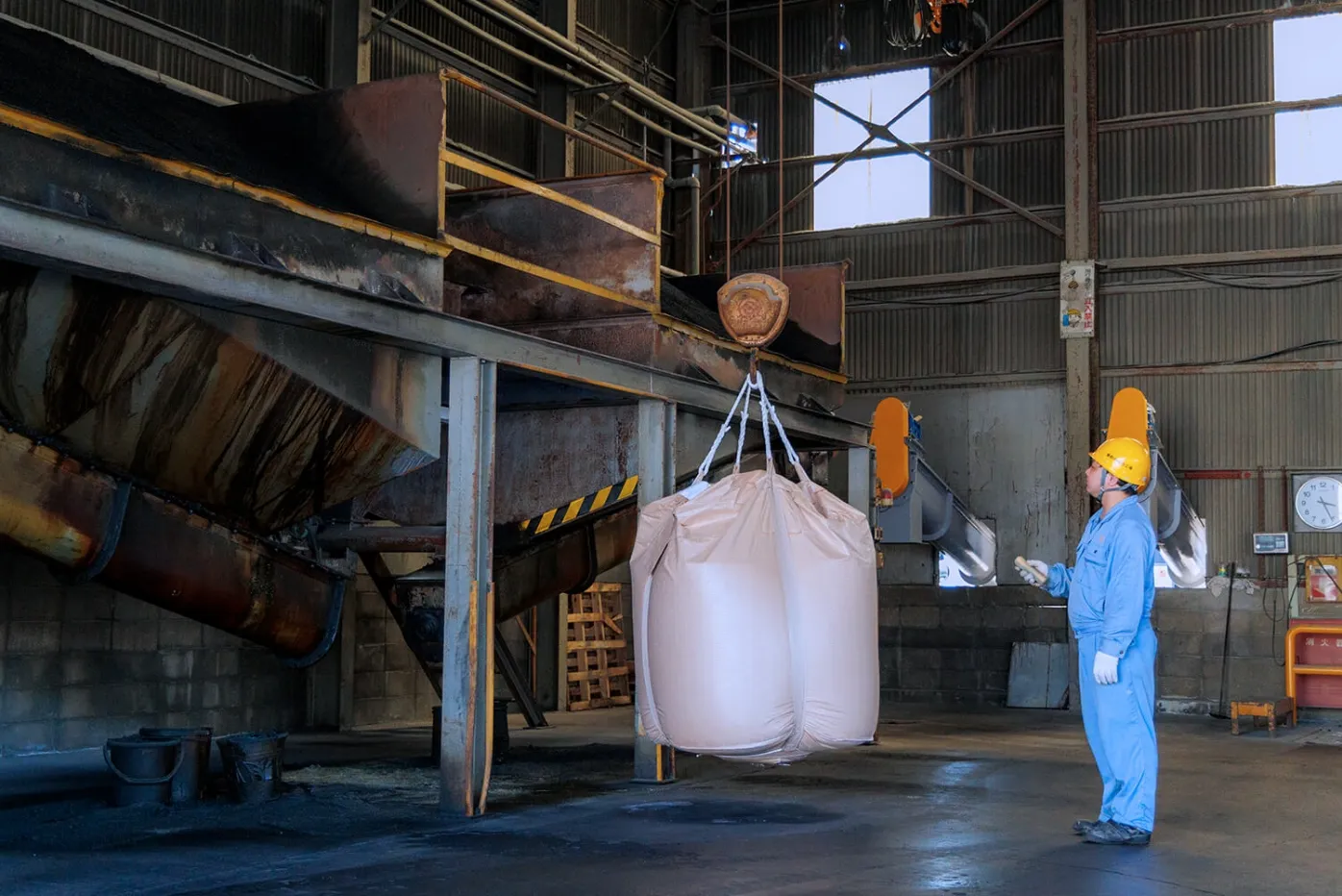 工場内でクレーンを使いフレコンバッグを移動させる作業員