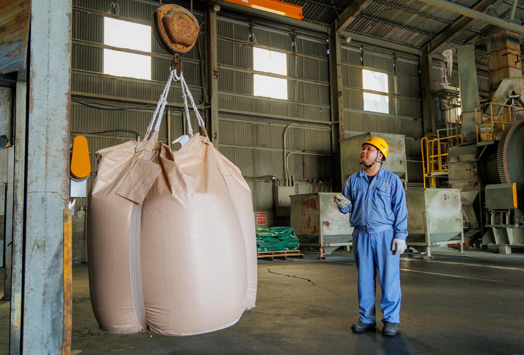 工場内でクレーンを使いフレコンバッグを移動させる男性社員
